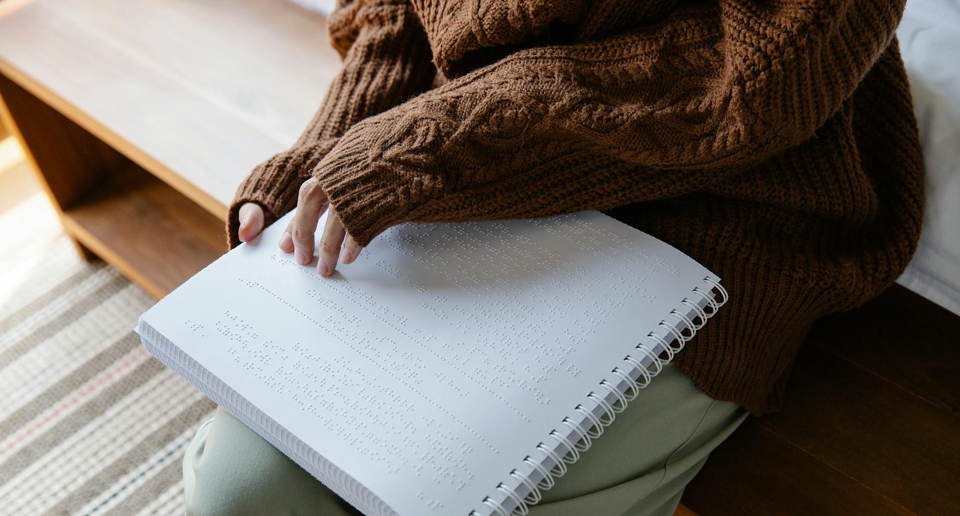 Osoba w swetrze czyta książkę w alfabecie Braille’a dłonią