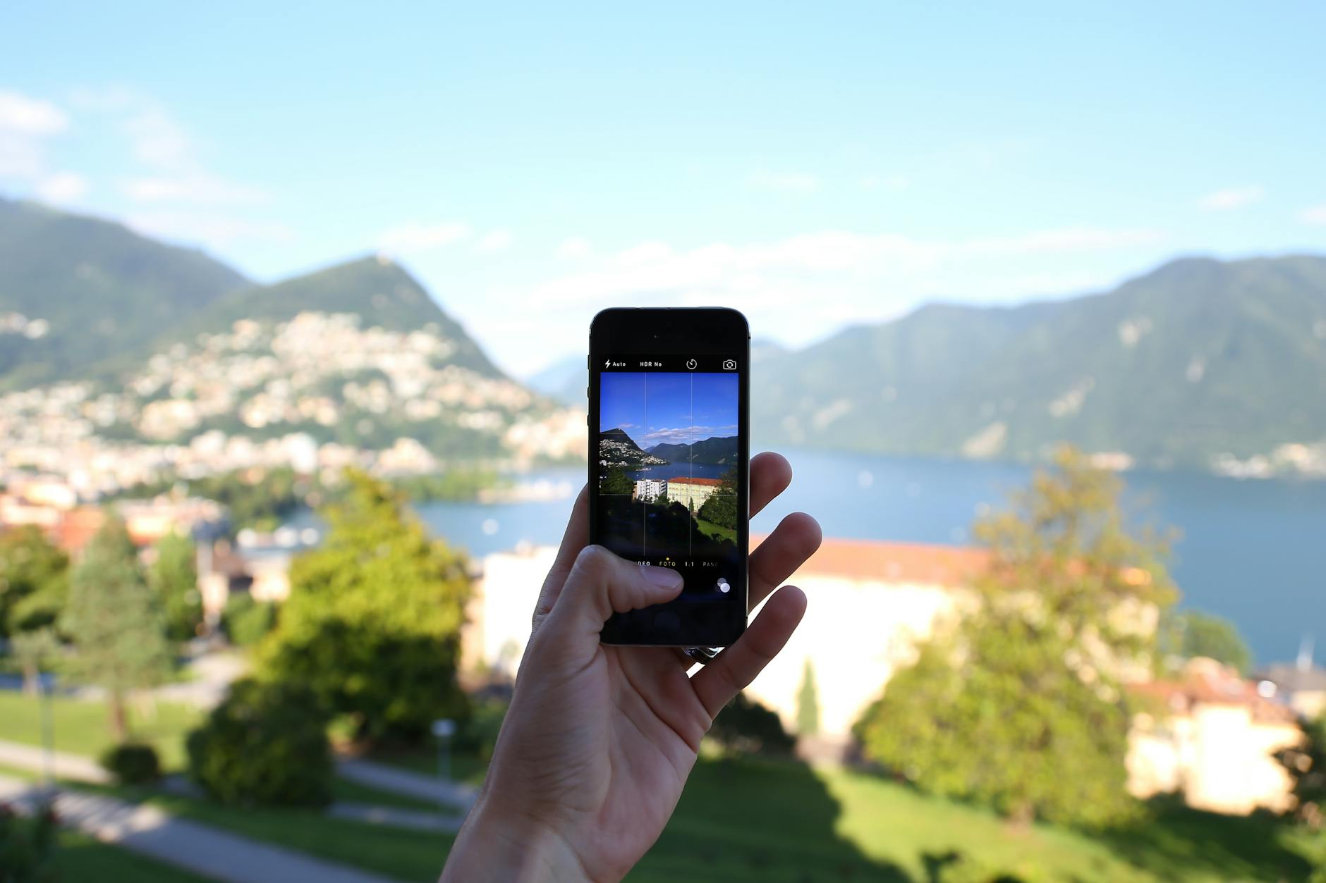 Osoba robiąca zdjęcie jeziora smartfonem, w tle góry i zabudowania