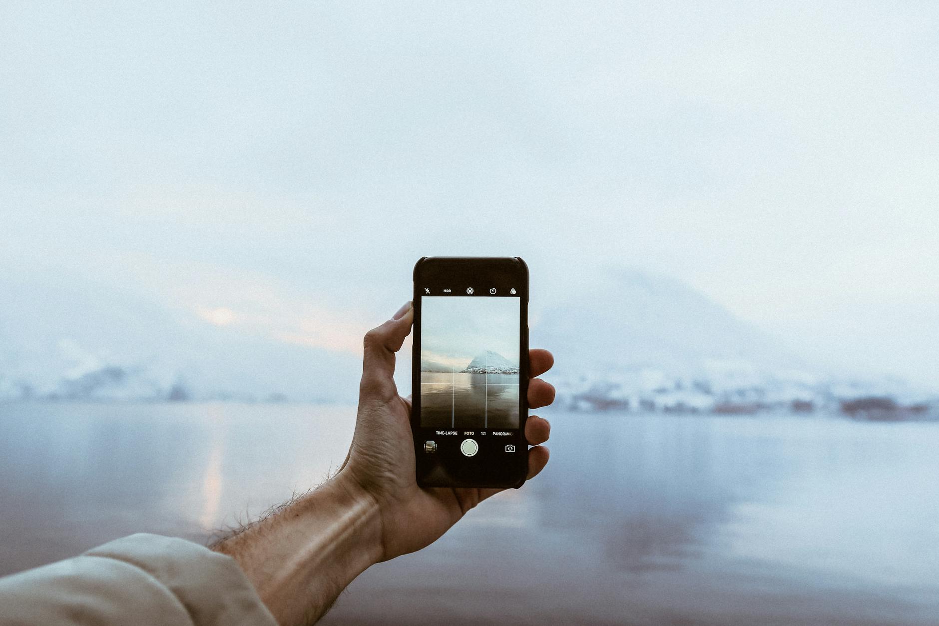 Osoba robiąca zdjęcie smartfonem ośnieżonych gór nad jeziorem