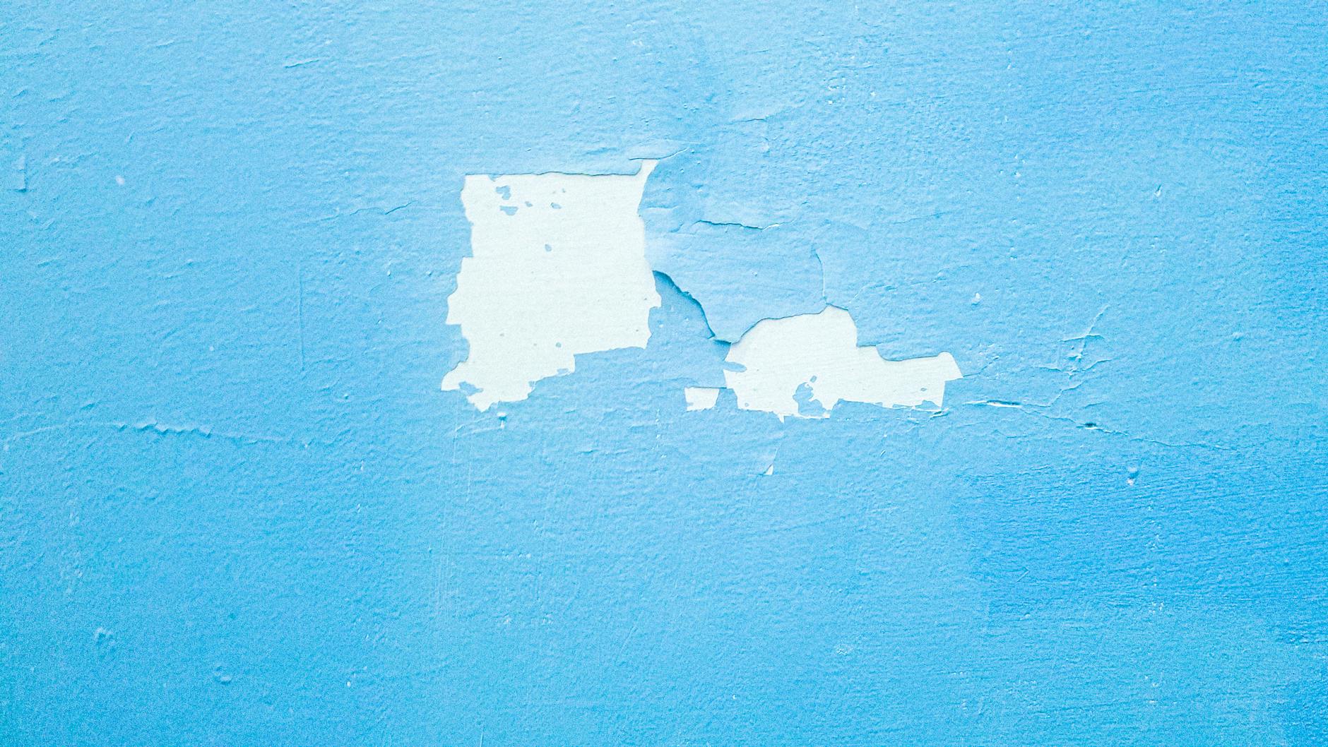 Zbliżenie niebieskiej ściany z łuszczącą się farbą i pęknięciami tynku