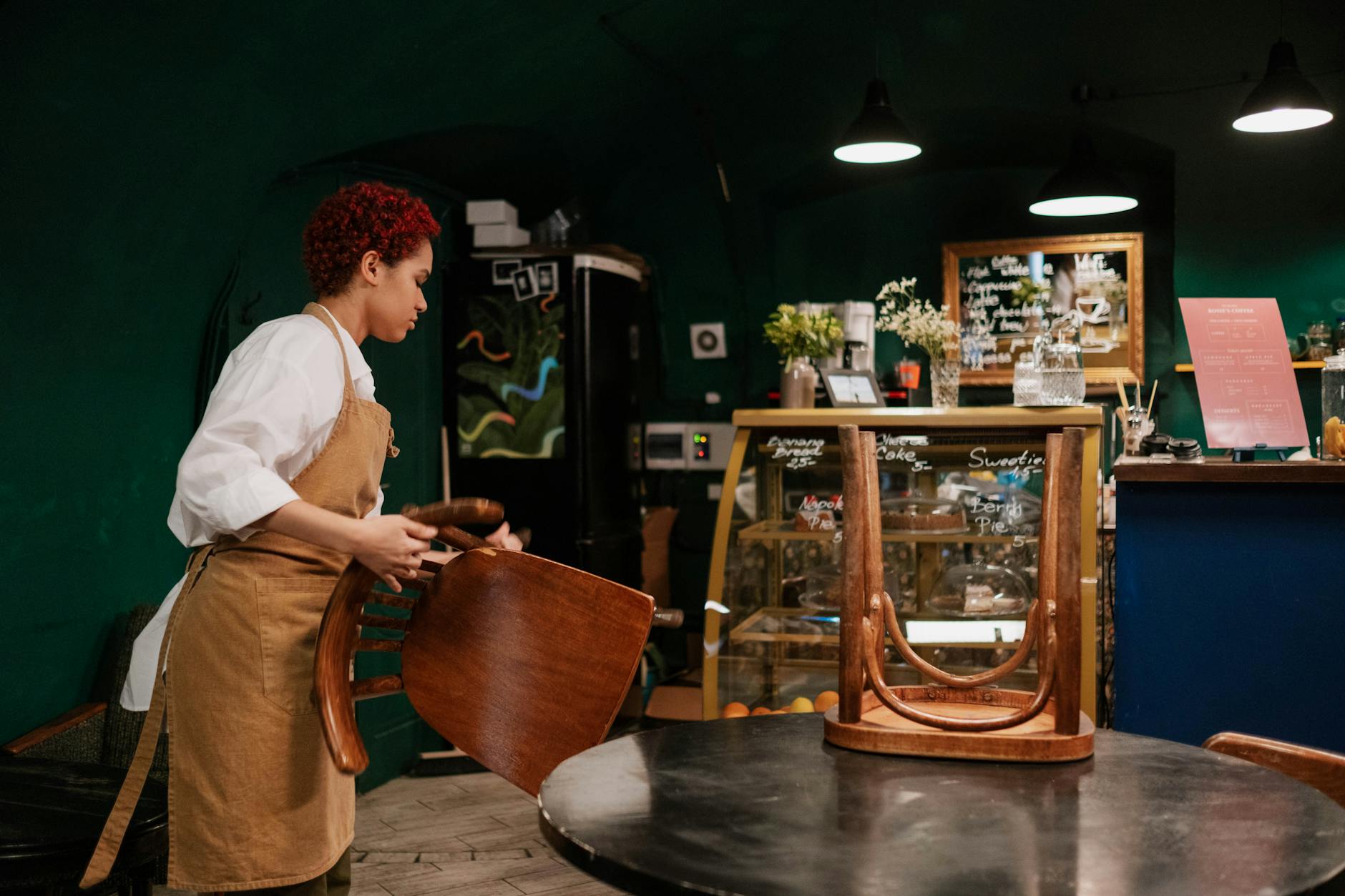 Kelnerka porządkuje przytulną kawiarnię z drewnianymi krzesłami