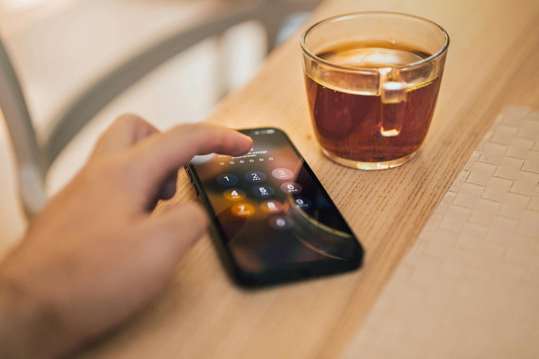 Dłoń odblokowująca smartfon leżący obok kubka herbaty na drewnianym stole