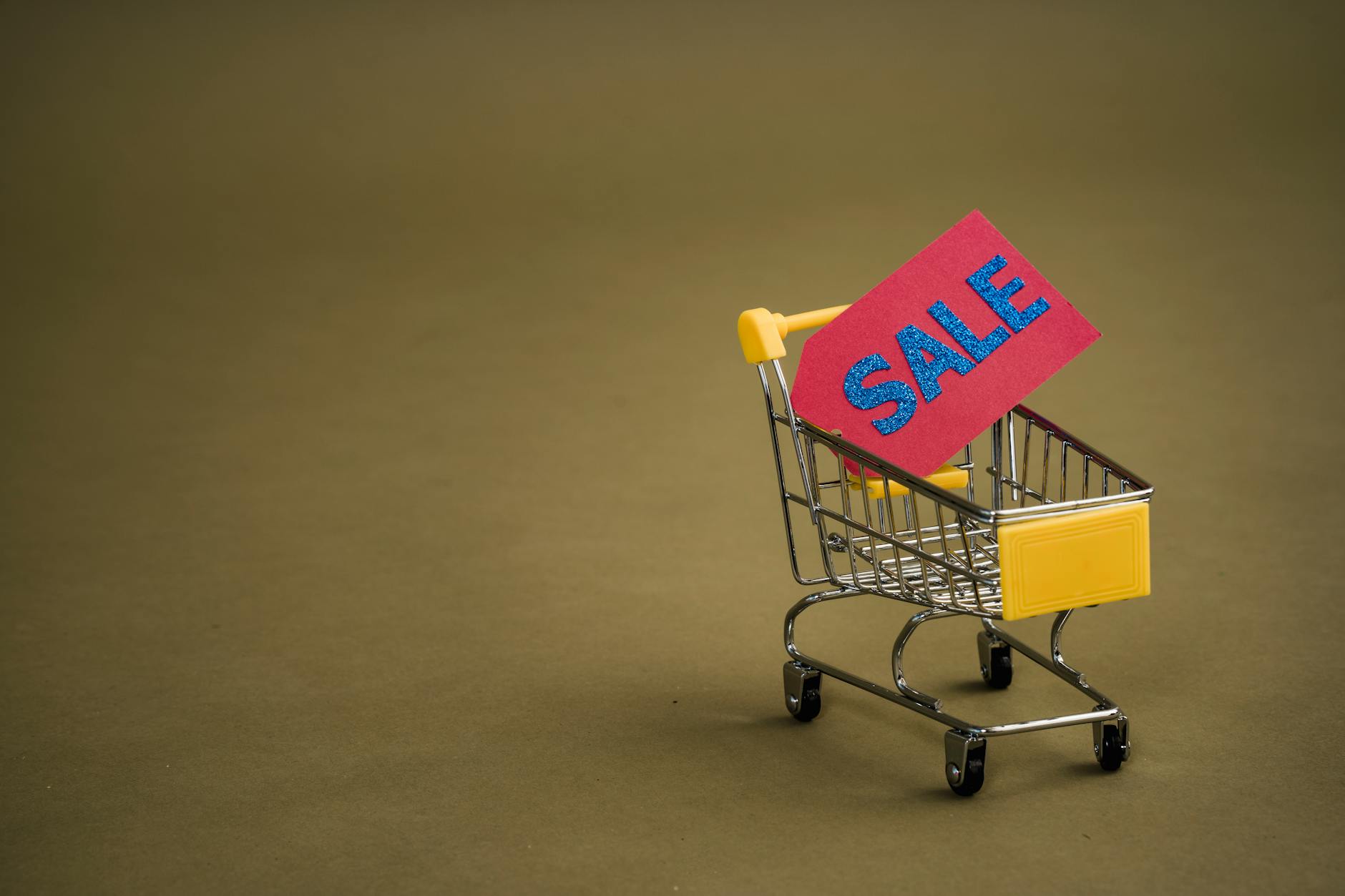 Miniaturowy wózek sklepowy z czerwonym napisem SALE na brązowym tle