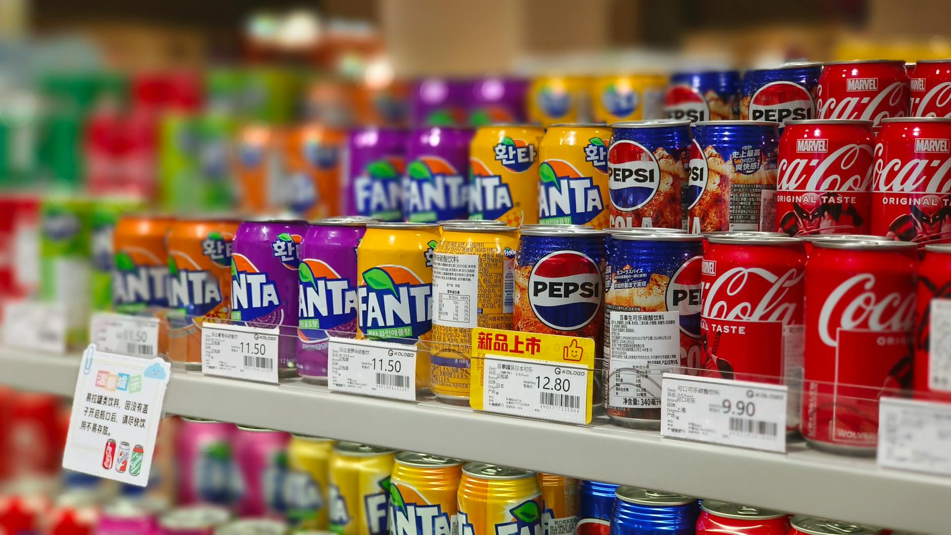 Puszki napojów Fanta, Pepsi i Coca-Cola na sklepowej półce z cenami