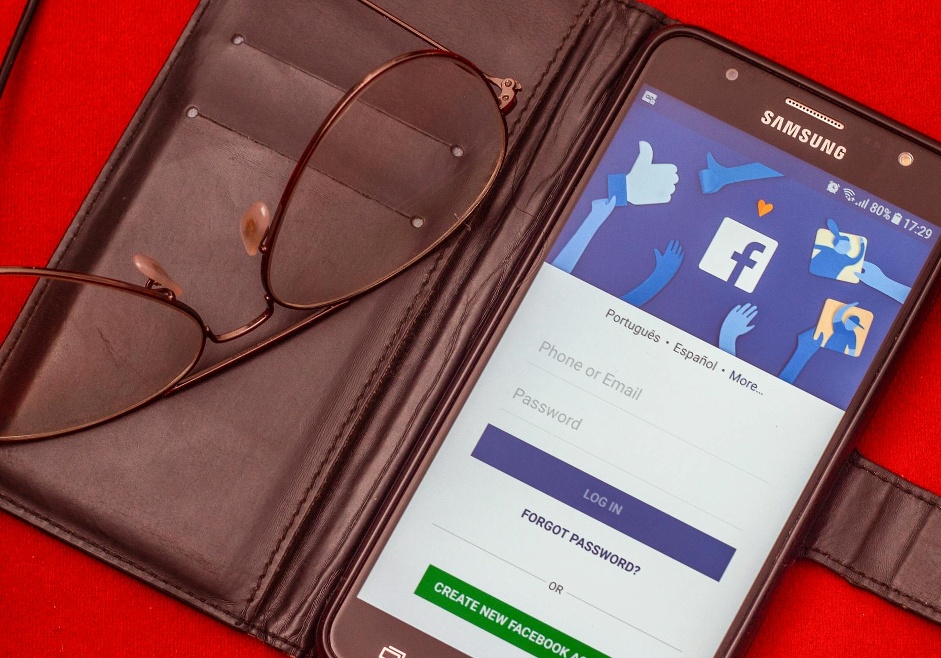 Smartfon z ekranem logowania Facebook obok okularów na czerwonym tle