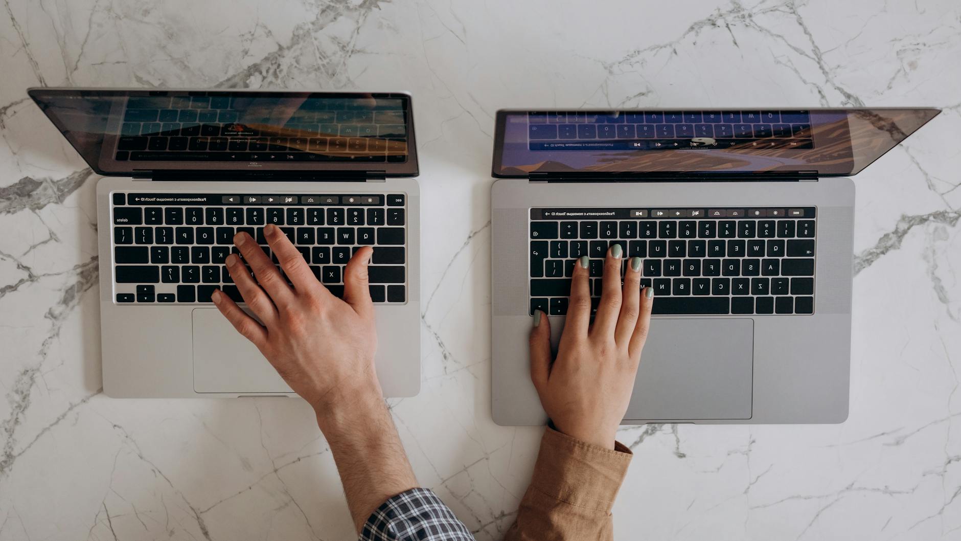 Dwie osoby piszą na klawiaturach laptopów, widok z góry