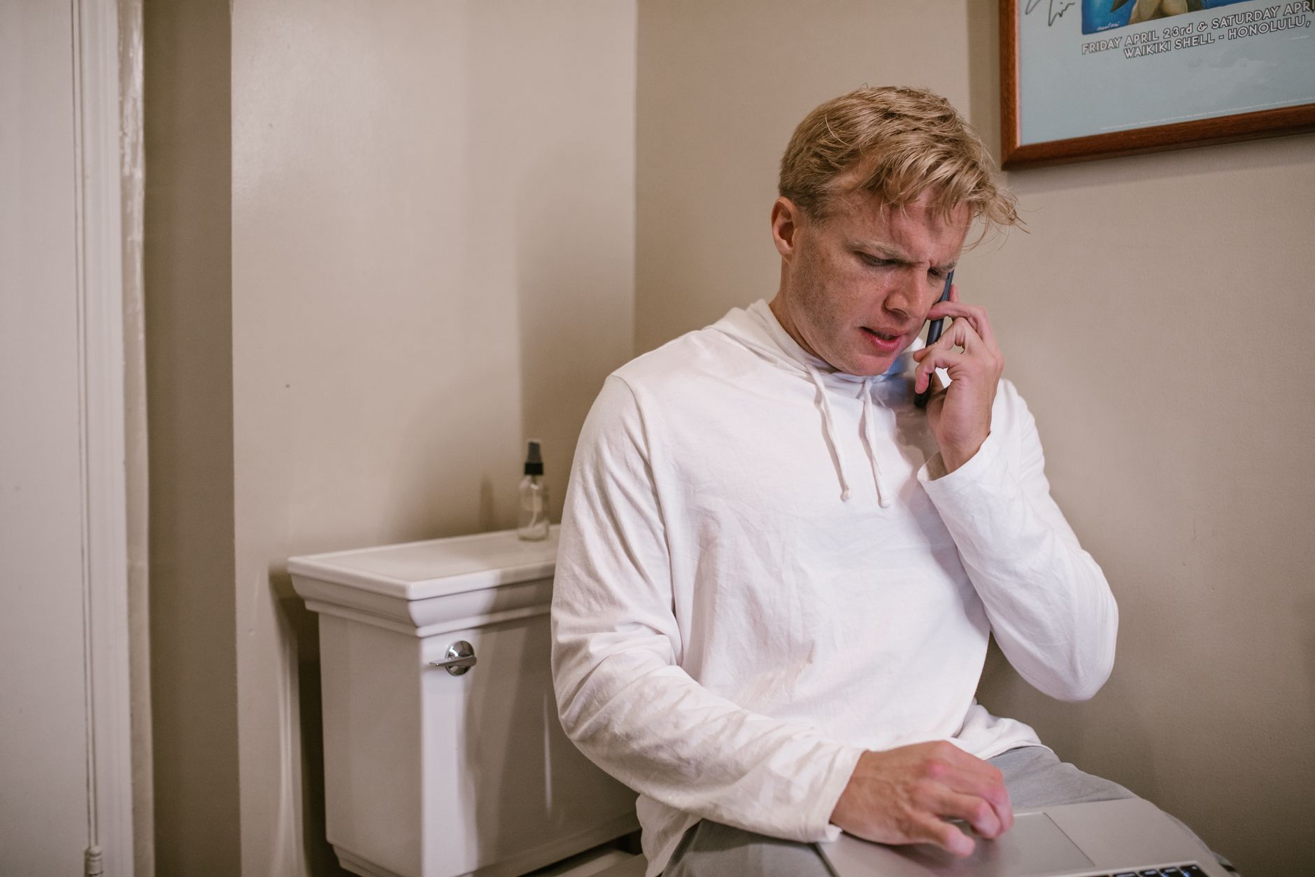 Mężczyzna w łazience korzysta z telefonu i laptopa obok toalety