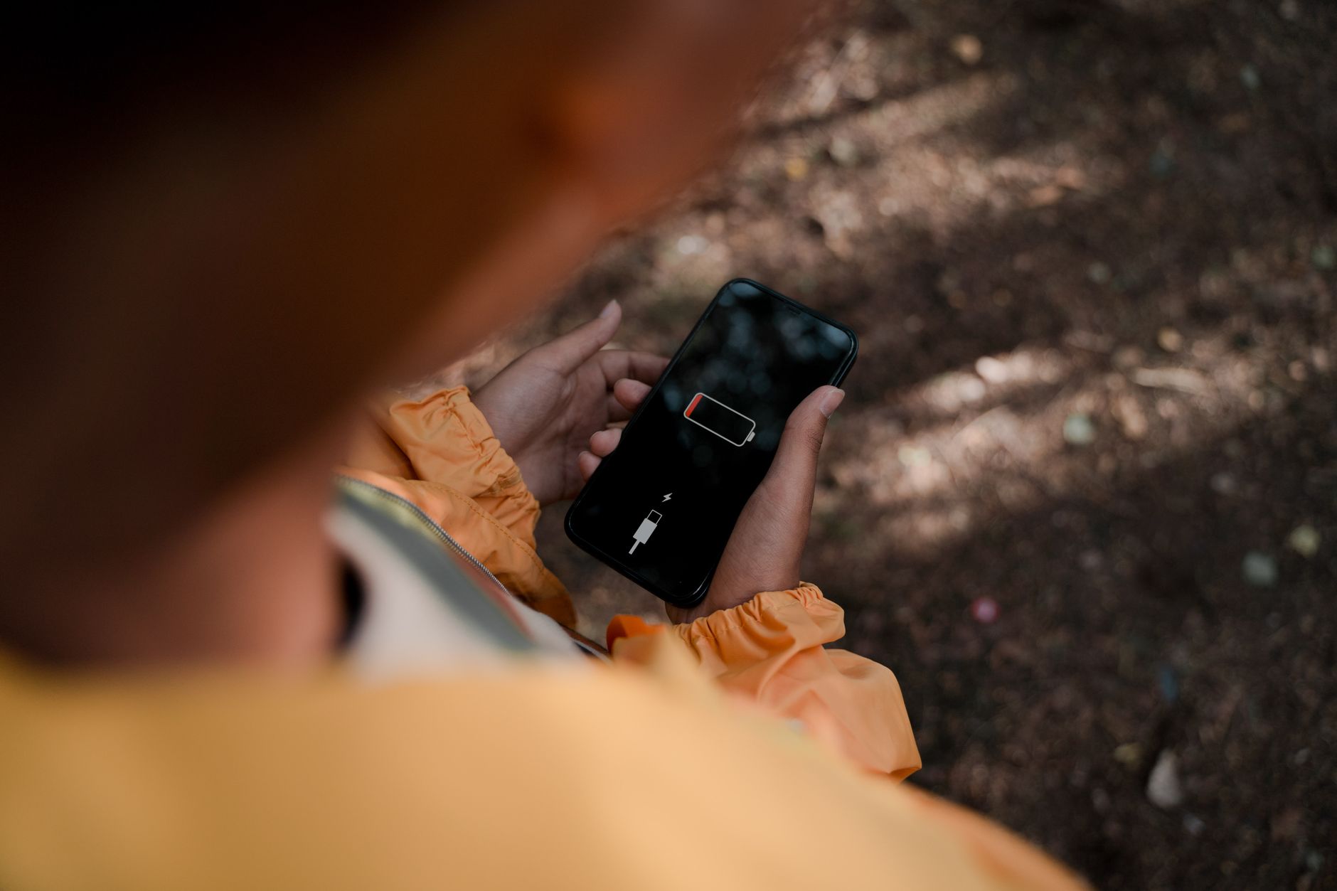 Nastolatek w lesie trzyma telefon z ikoną niskiego poziomu baterii